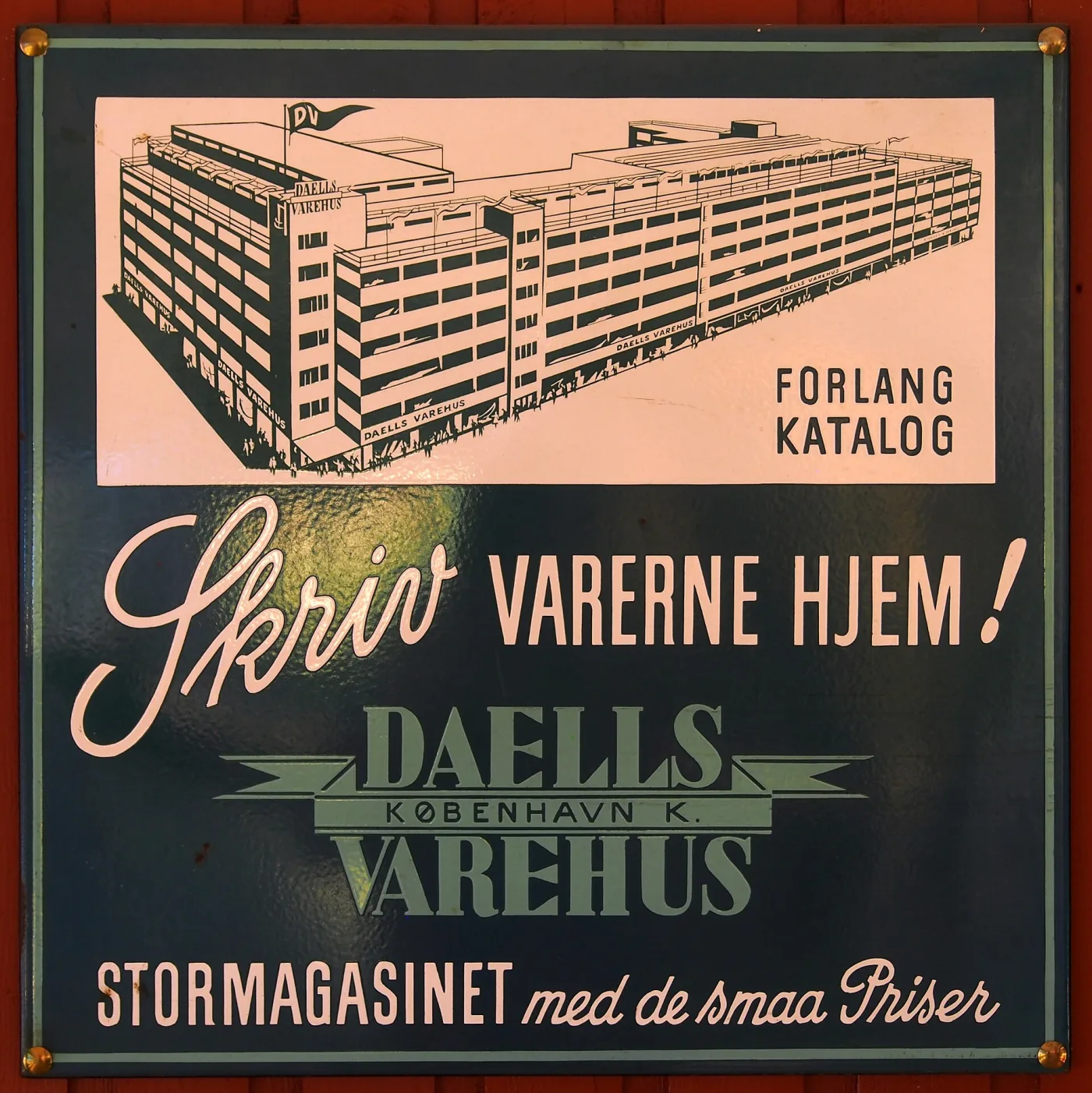 The same advertisement on a dark green ground with the building rendered in pale pink, lettered Forlang Katalog above and Stormagasinet med de smaa Priser below