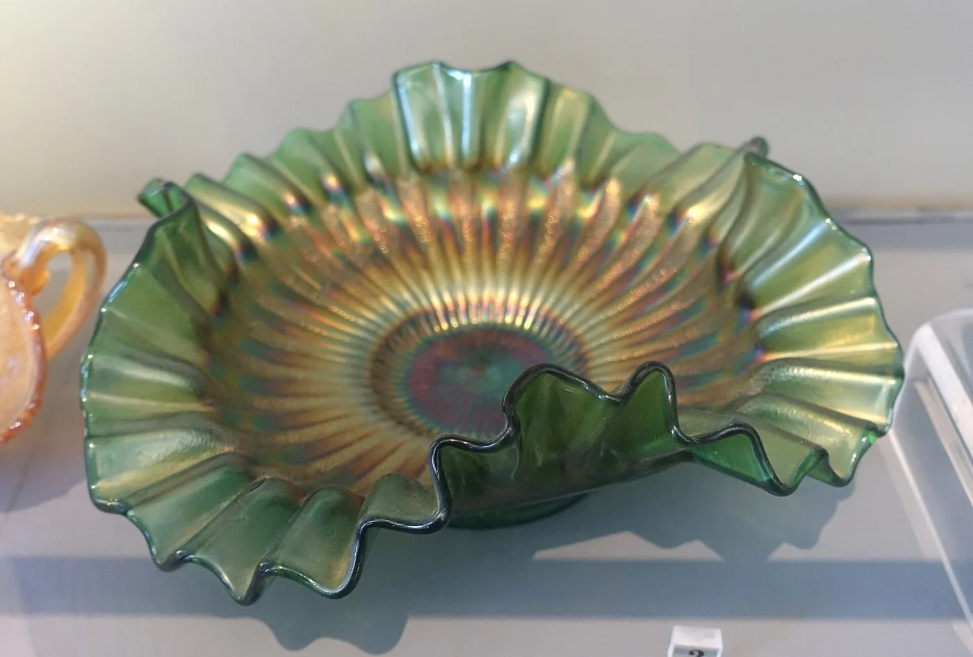 Carnival glass bowl with a wide ruffled rim and radiating moulded ribs, green at the edge and iridised to gold and violet towards the centre