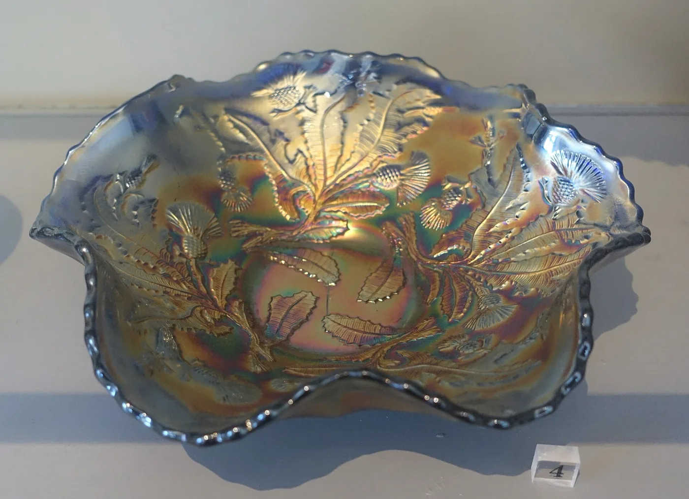 Carnival glass bowl with a deeply ruffled and crimped rim and a moulded thistle-and-leaf pattern, its surface breaking into oil-slick blues, violets and gold