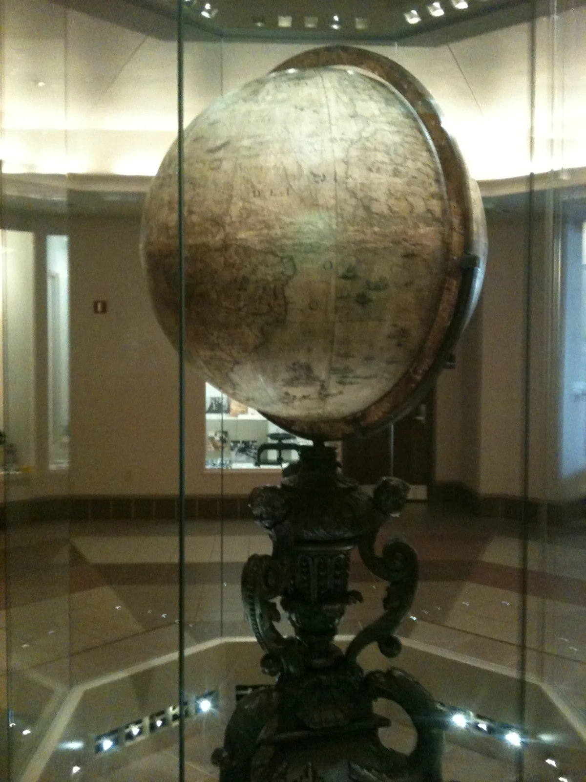 Very large dark blue terrestrial globe on an ornate carved stand, displayed behind glass in a wood-panelled library room