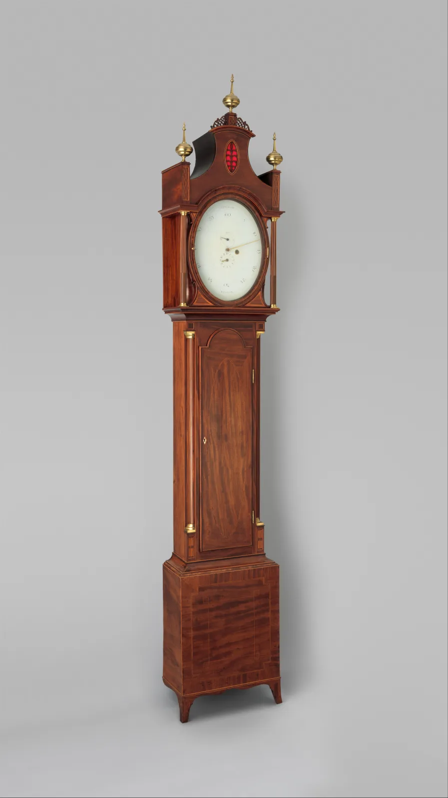 Longcase clock in figured mahogany with a swan-neck pediment above an arched white painted dial with black numerals and a painted scene in the arch, over a long trunk door and a shaped plinth