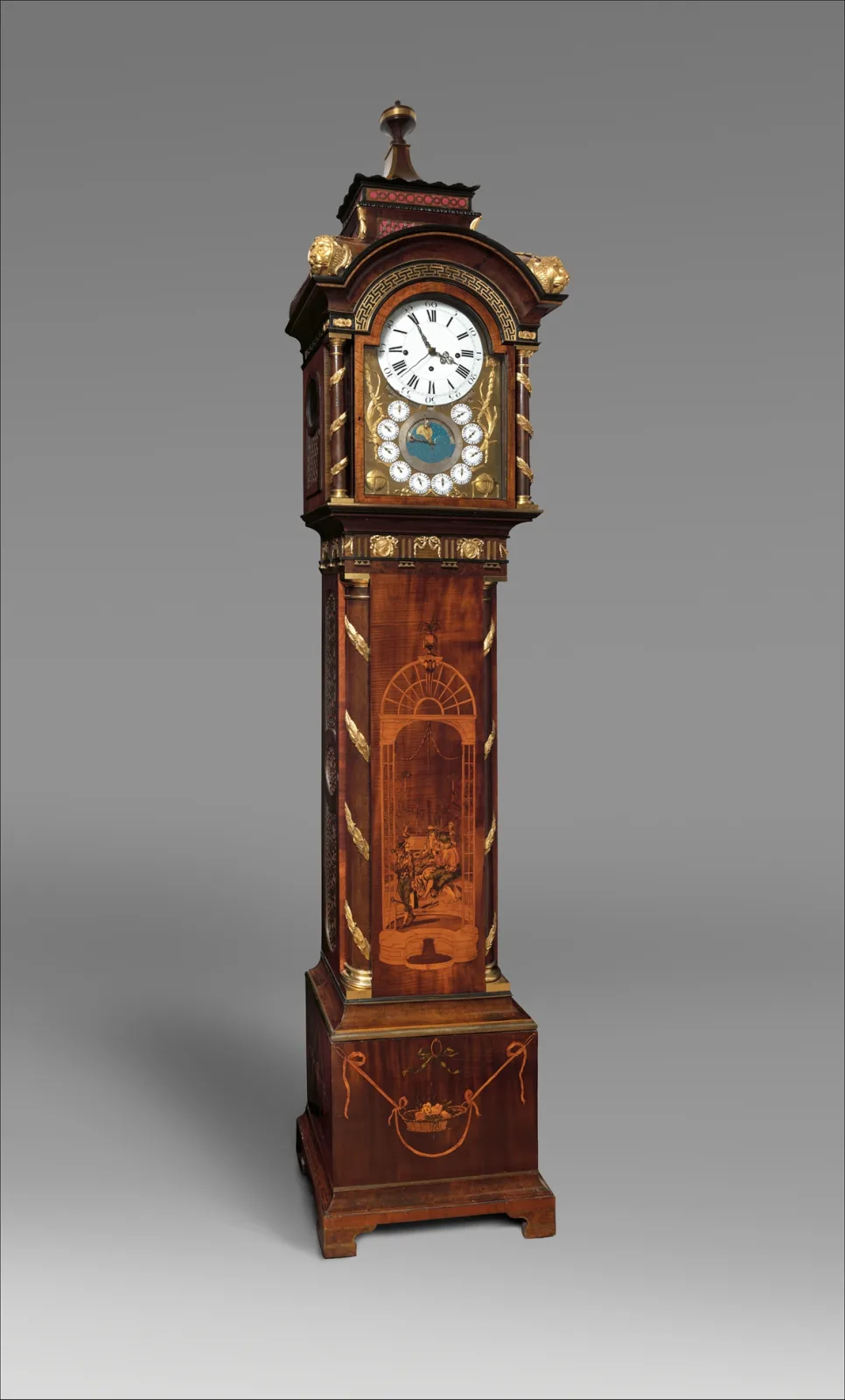 Tall clock case in marquetry-inlaid wood with a domed and finialled hood, a glazed arched dial door and a slim tapering trunk with inlaid panels, on a moulded plinth