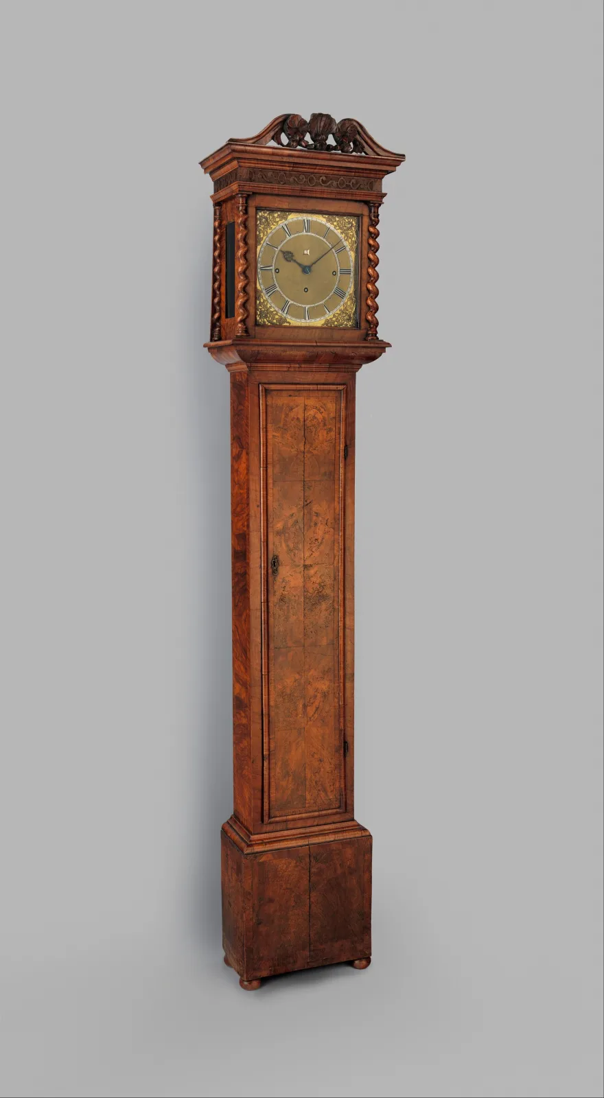 Longcase clock with a tall narrow case, a flat-topped hood with a moulded cornice, a square brass dial with a silvered chapter ring and a calendar aperture, above a plain trunk and base