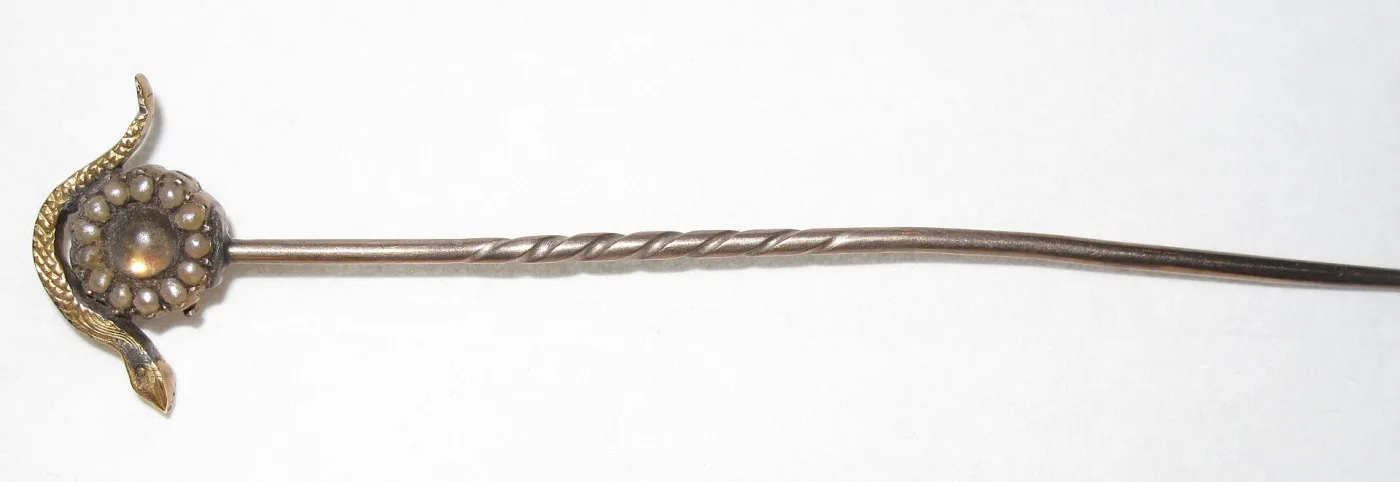 Hat pin head of a gold snake coiled around a domed boss ringed with seed pearls, on a shaft twisted along part of its length