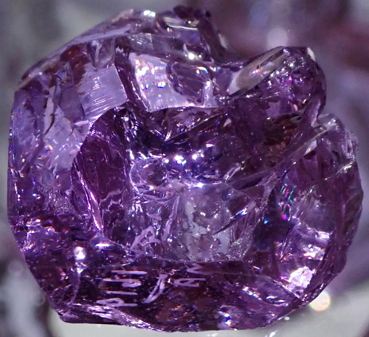 A rough lump of lavender glass with fractured, glassy faces, photographed close up