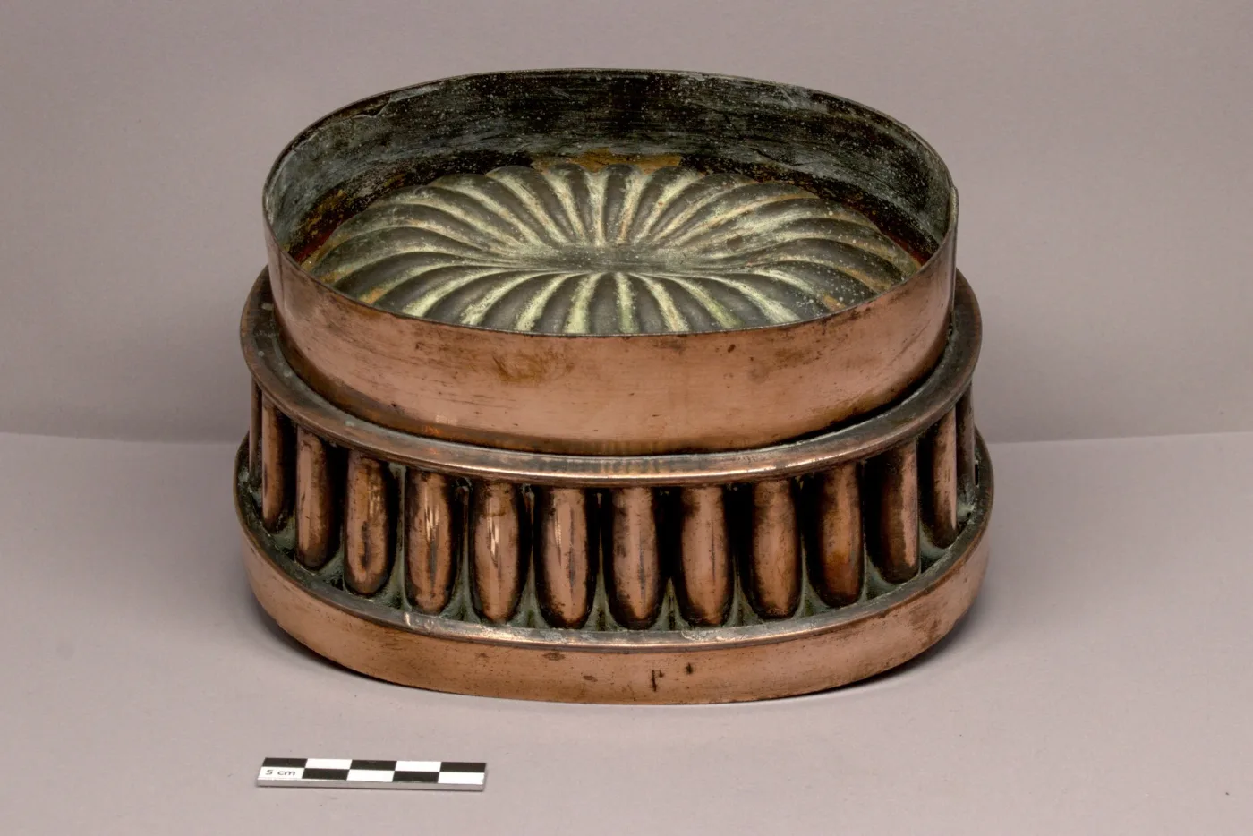 Oval copper sorbet mould with a band of raised flutes around the body, its lid missing, the lined interior showing a fan-shaped rosette
