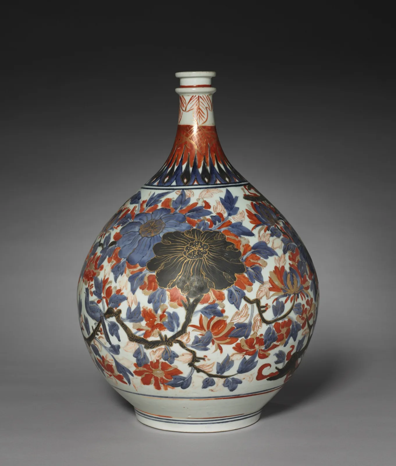 Bulbous Arita porcelain bottle with a tall narrow neck, painted in underglaze blue and iron red with a dense pattern of stylised chrysanthemum heads and scrolling foliage over the whole body