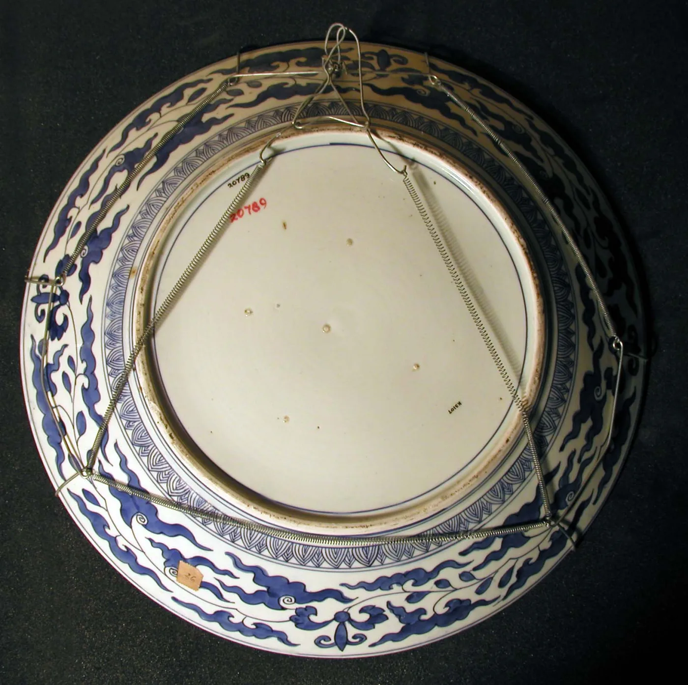 The reverse of the same charger, showing a broad footring, a plain glazed centre, sprays of blue foliage spaced around the underside and a wire hanging fitting stretched across the back