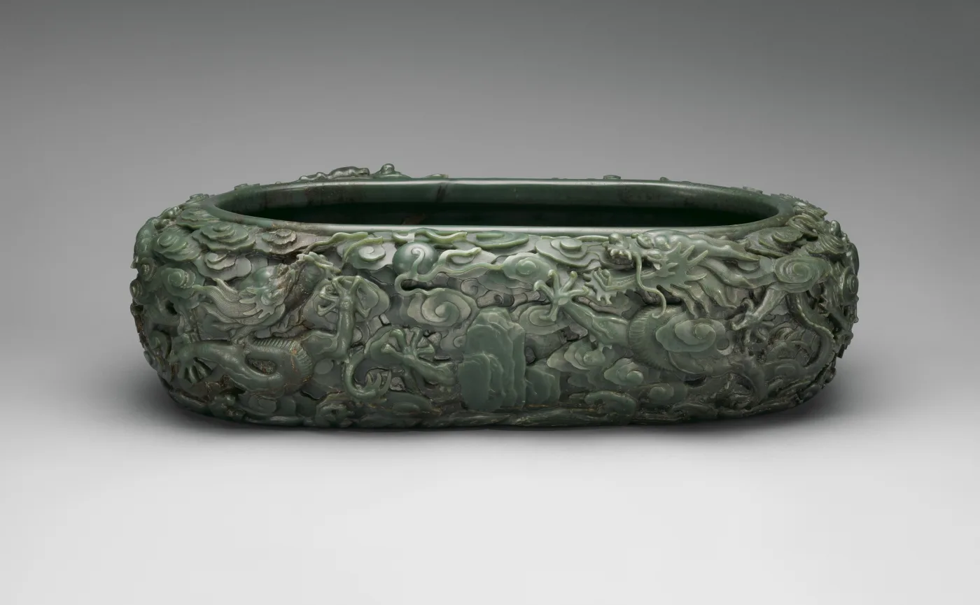 Large oval basin of dark green stone carved in high relief with dragons among clouds and waves