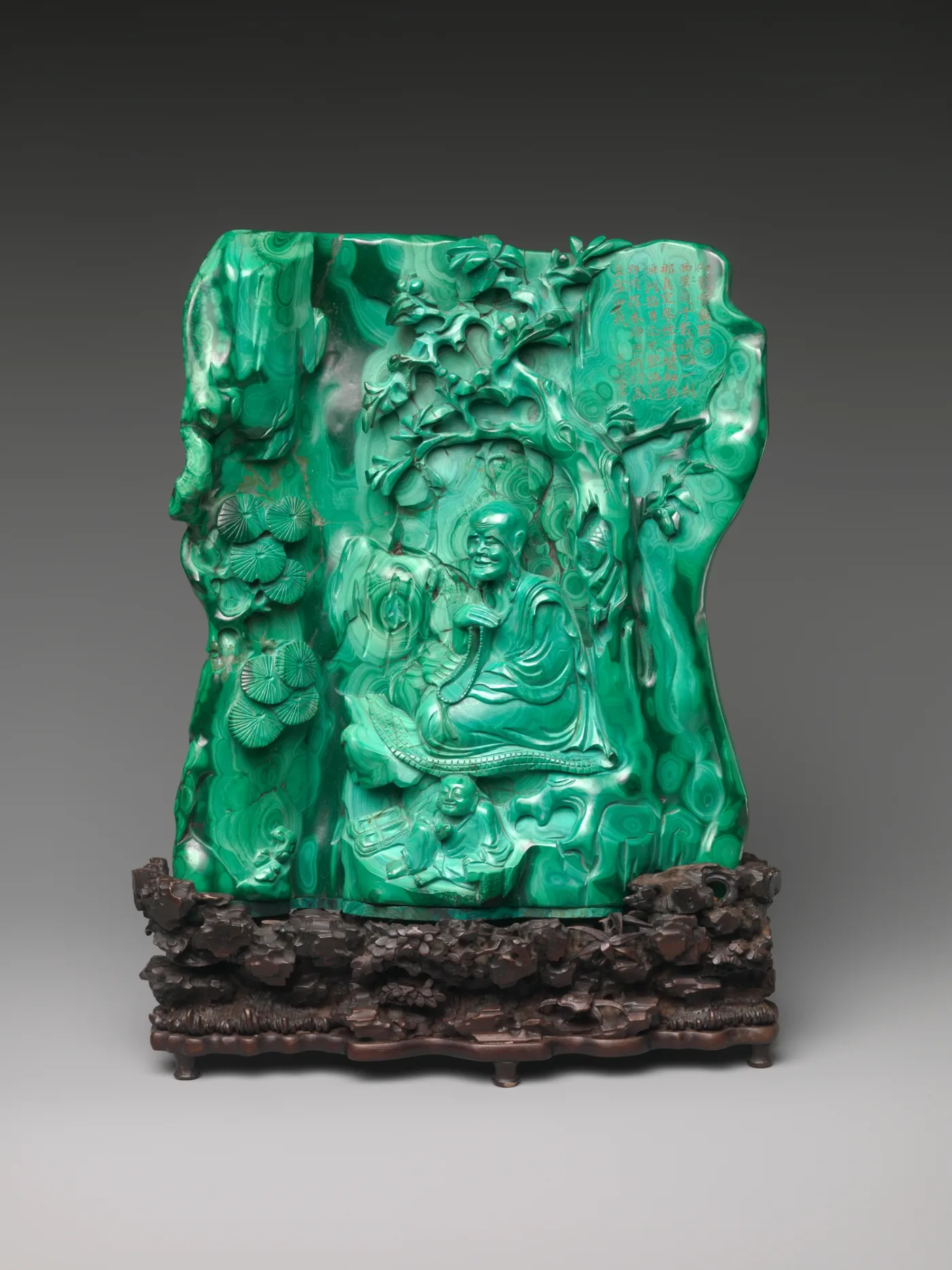 Standing figure of a monk holding a bowl, carved in banded green stone with concentric ring patterning