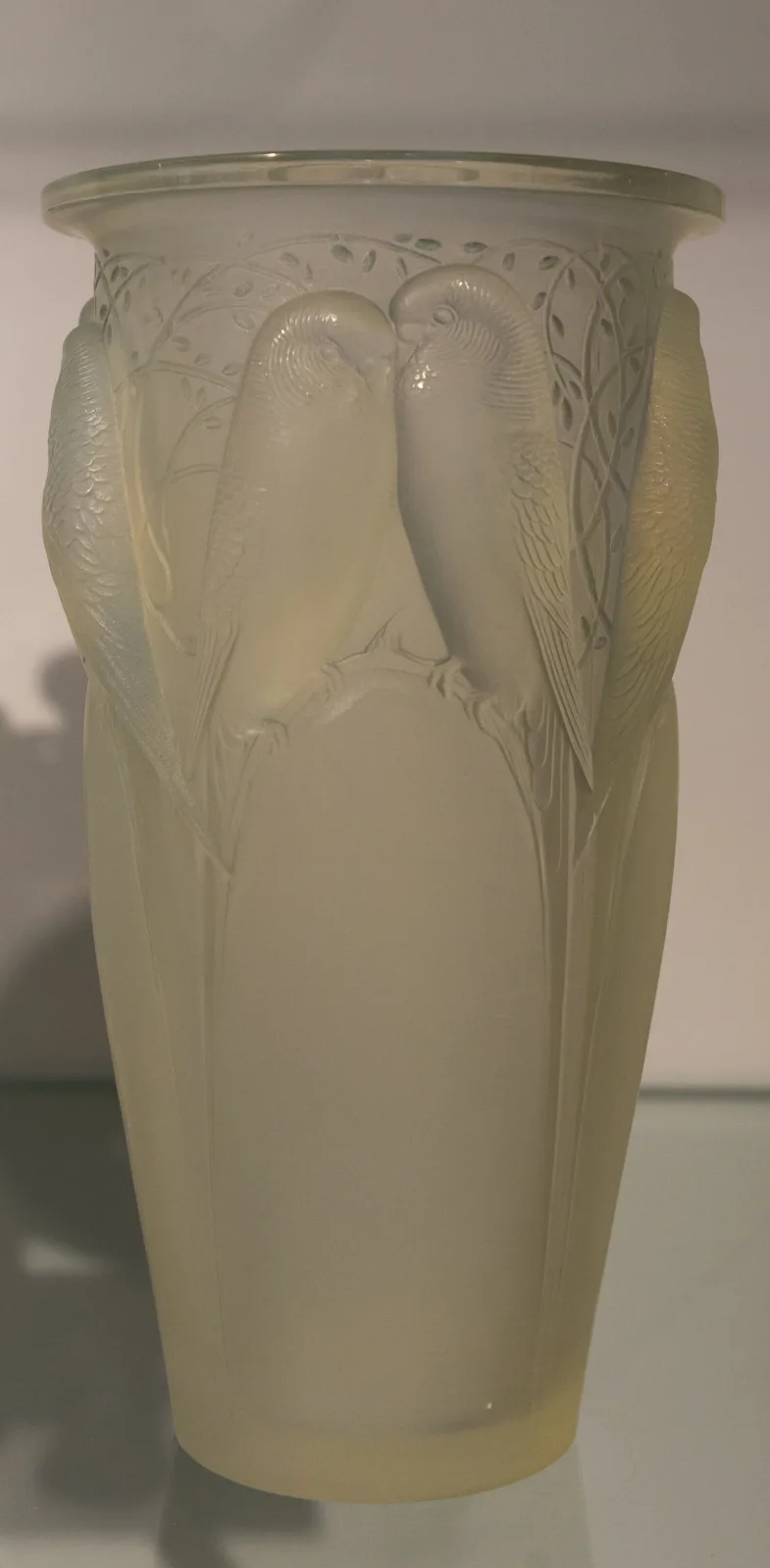 Tall vase moulded with pairs of budgerigars perched among branches, the glass milky white and shading to a blue tint where the relief is thickest
