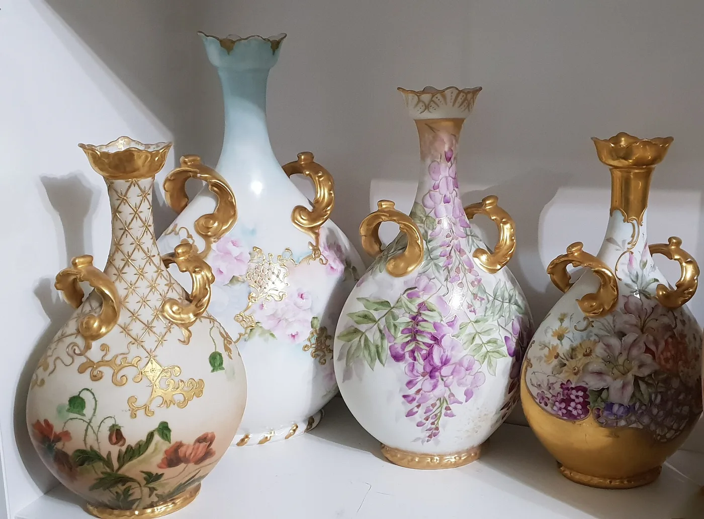 Four antique Limoges porcelain vases with gilded scroll handles, hand-painted with wisteria, poppies, roses and lilies