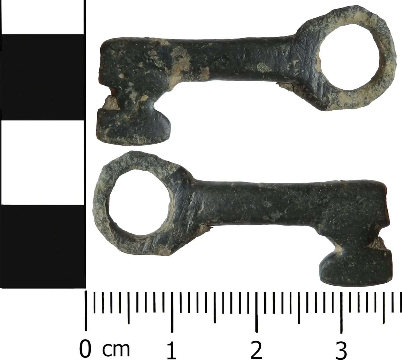Two views of a small medieval casket key with a broken shaft, the bit formed from a square plate cut with a pair of opposing semicircular notches, against a centimetre scale