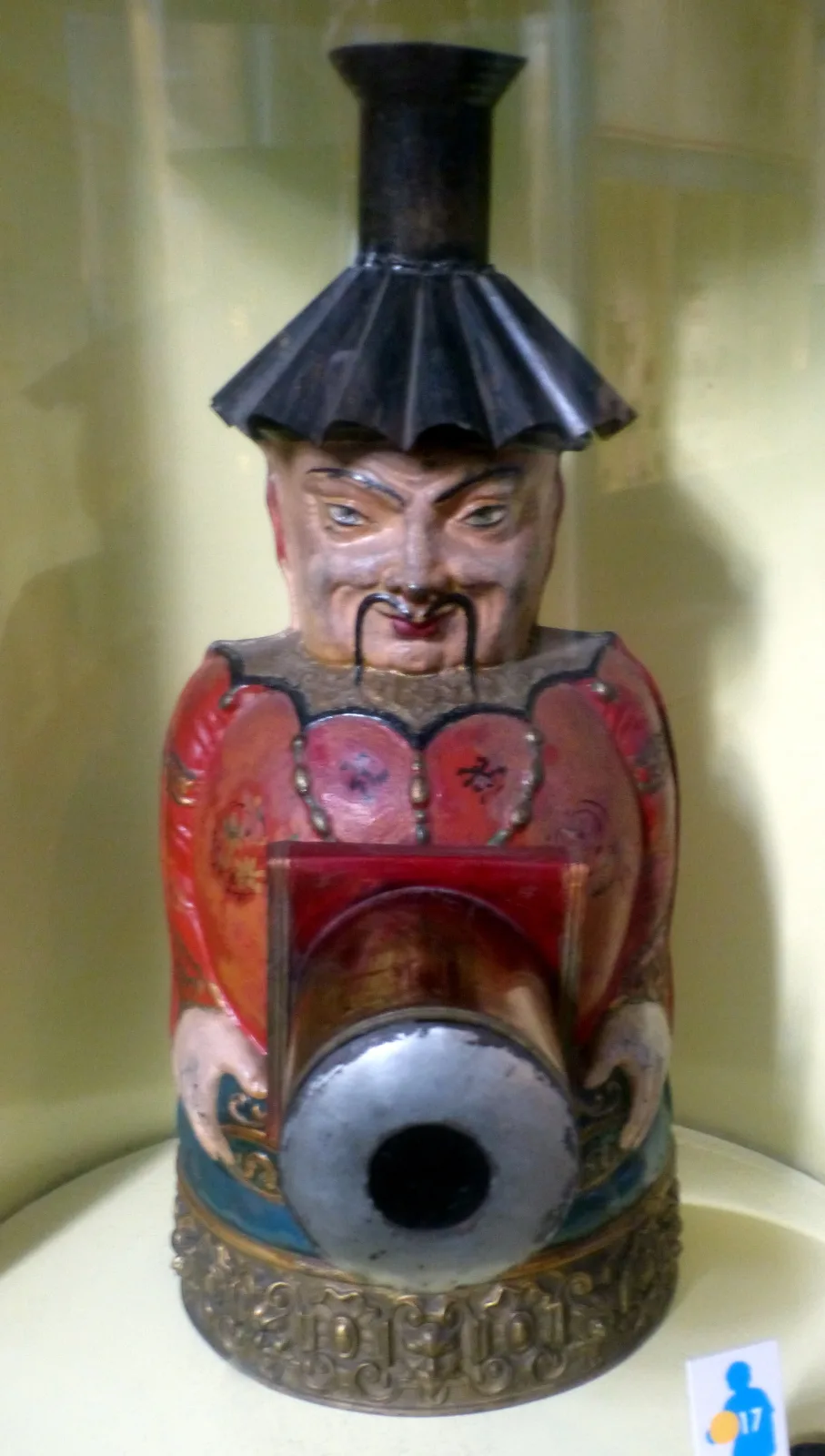 Novelty magic lantern moulded as the head and shoulders of a figure in a black hat and red robe, the lens projecting from the chest where a body panel would be, standing on a decorated round base