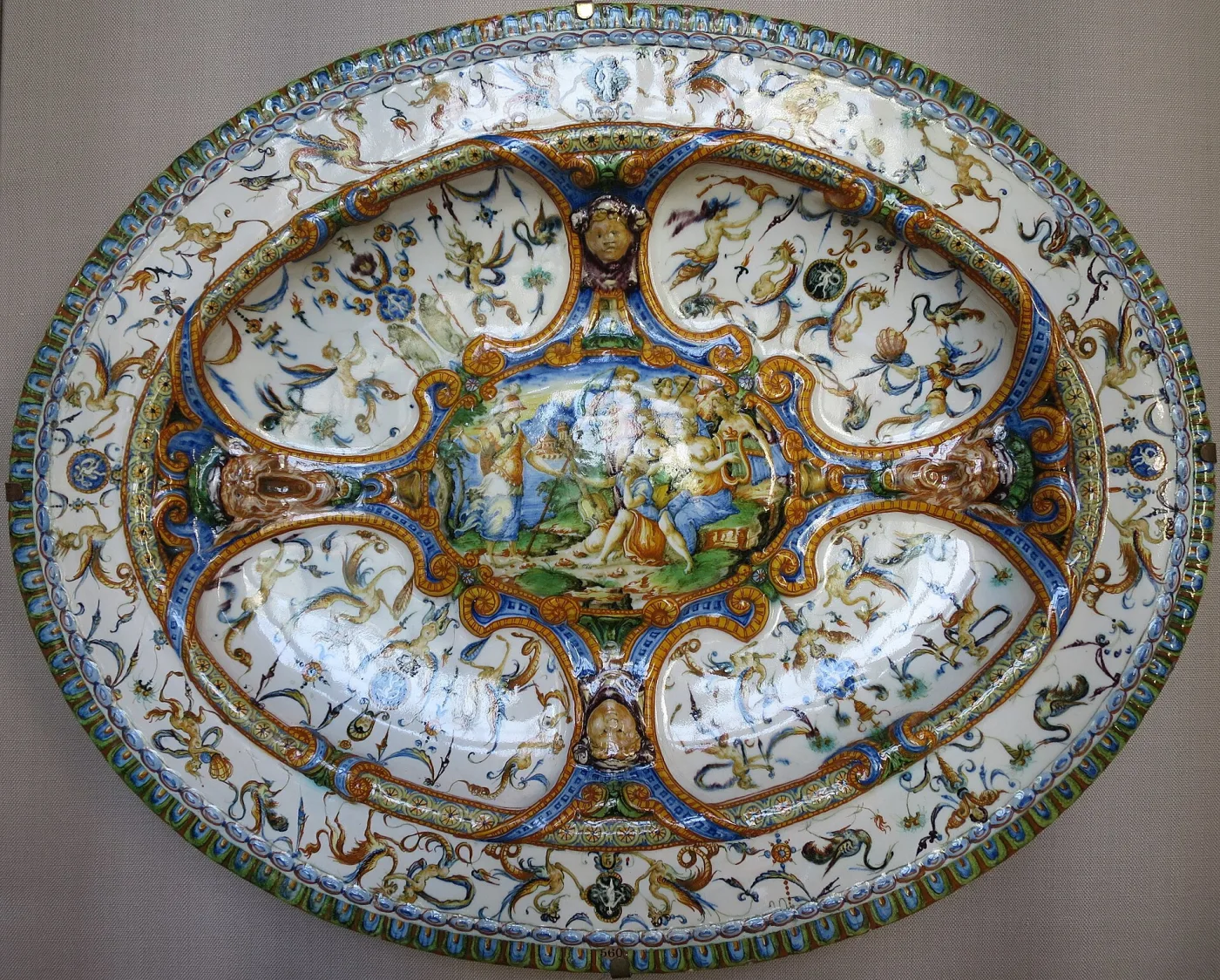 Wide dish painted across its whole surface with a scene of Minerva and the Muses in a landscape, in blue, orange and yellow on a white ground