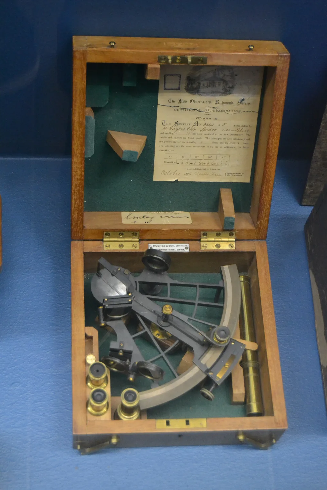 Sextant of blackened metal with a graduated arc, micrometer drum and a telescope, fitted into a shaped mahogany case with spare eyepieces and a printed certificate mounted inside the lid