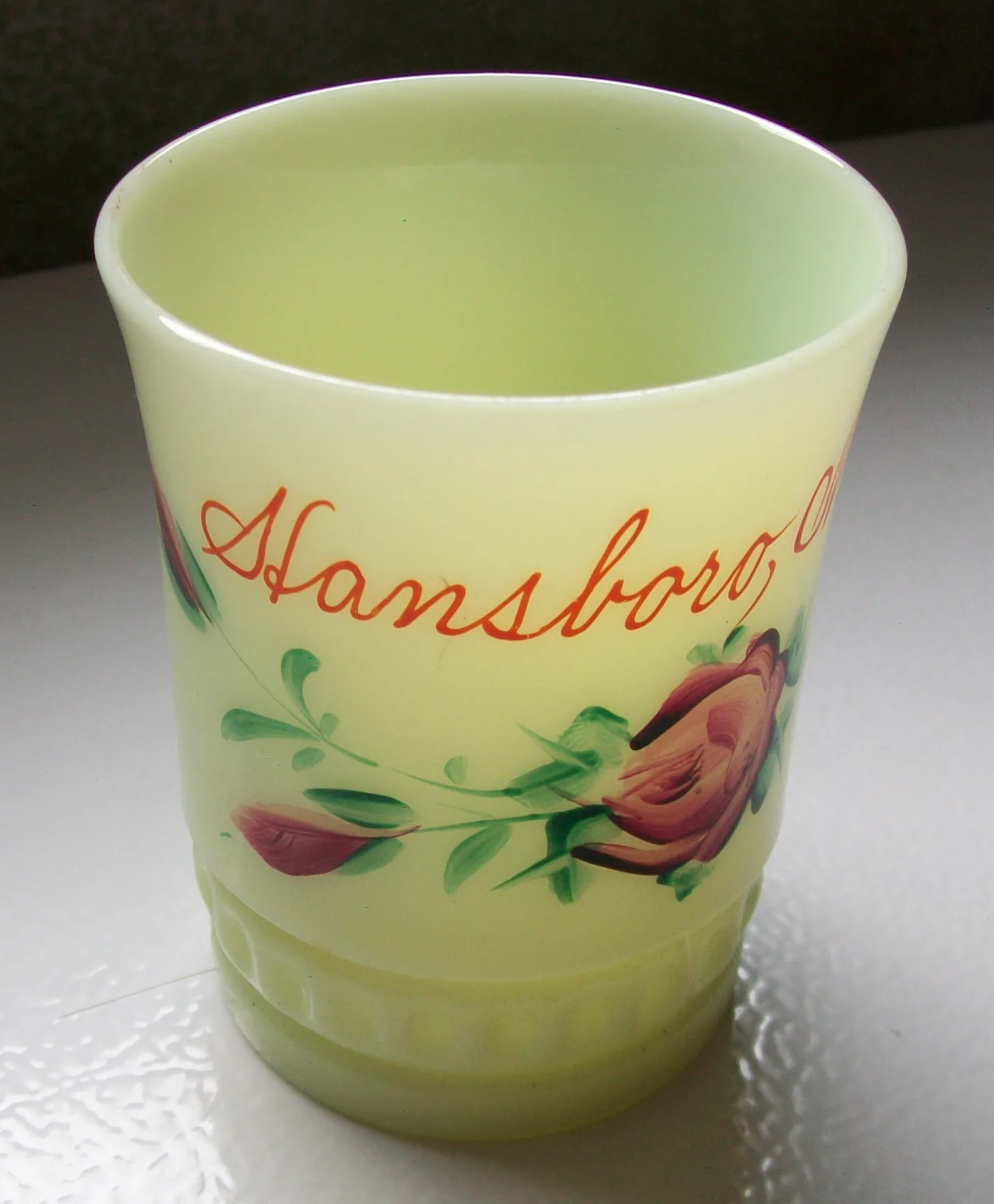Pale yellow-green opaque glass souvenir cup lettered Hansboro and painted with roses and green leaves