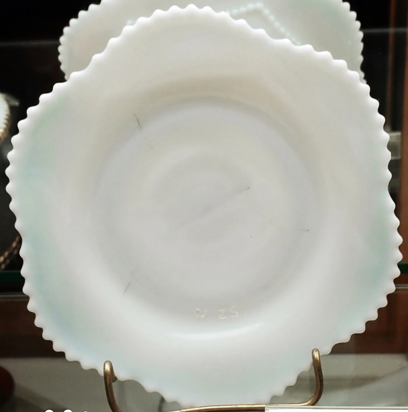 Round white milk glass plate with a sawtooth rim and faint moulded characters in the centre, on a wire stand