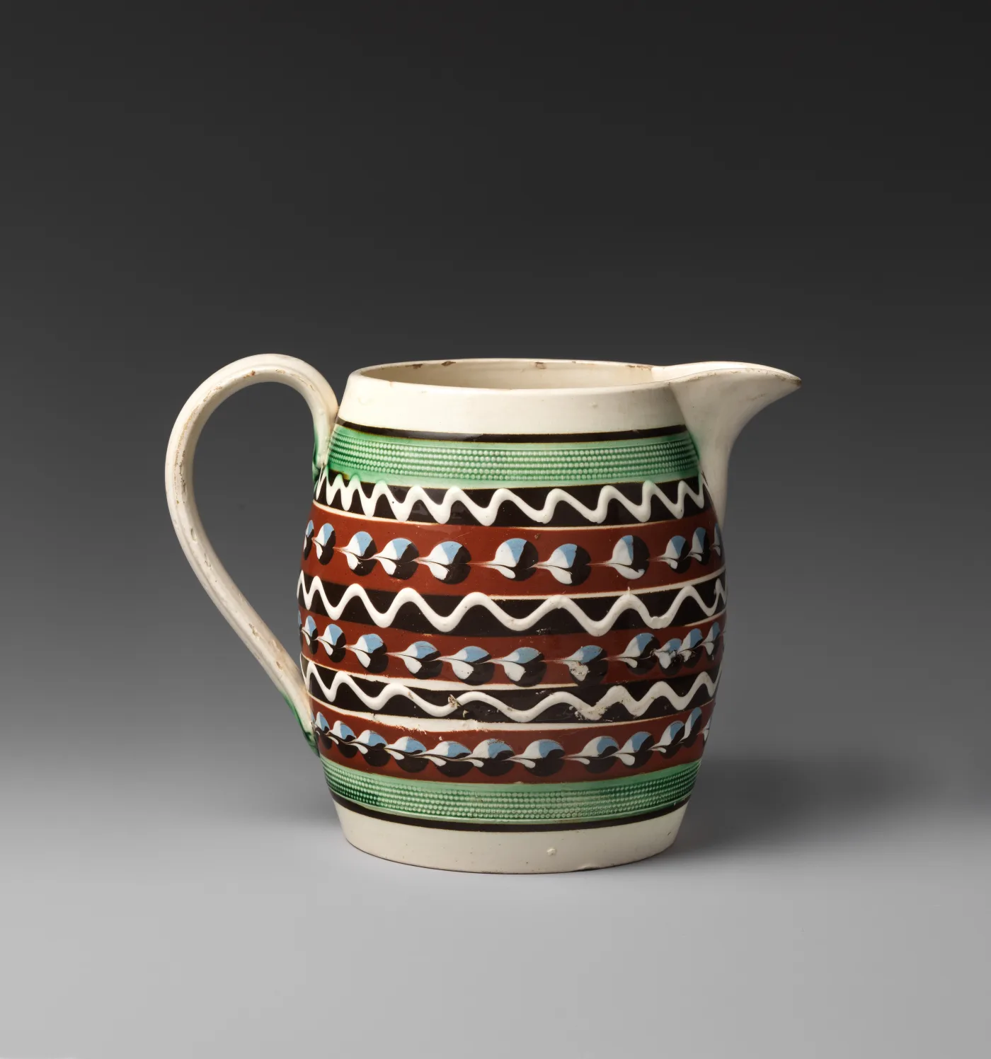 Barrel-shaped jug with a green ground band edged in white, carrying a bold zigzag of trailed brown and white slip between rows of dots