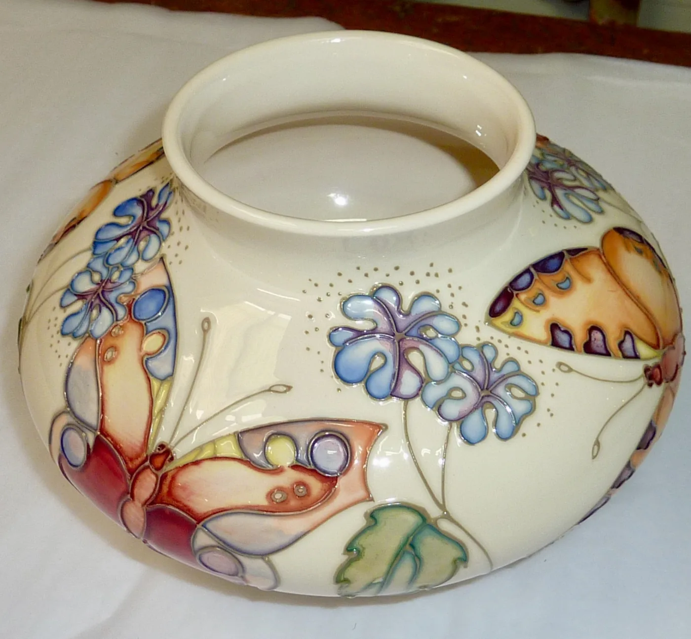 Wide squat vase with a pale cream ground, decorated with butterflies and blue flowers in soft washes, the outlines fine and light