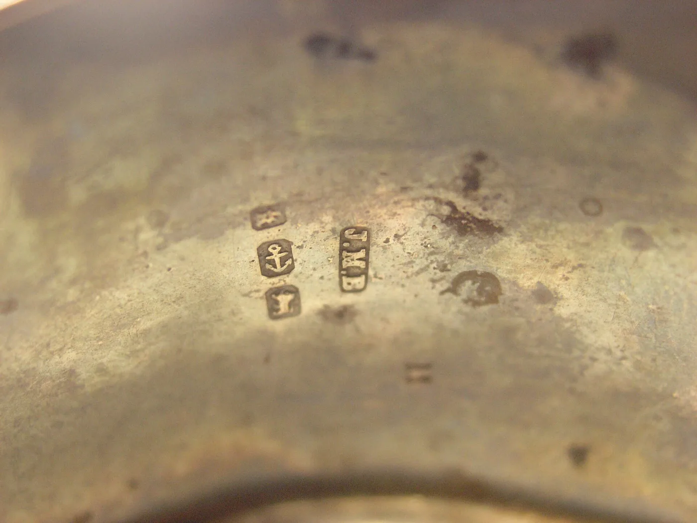 Four small struck marks on silver: an anchor, a lion, a letter in a shield, and the initials J.M.B in a rectangular punch