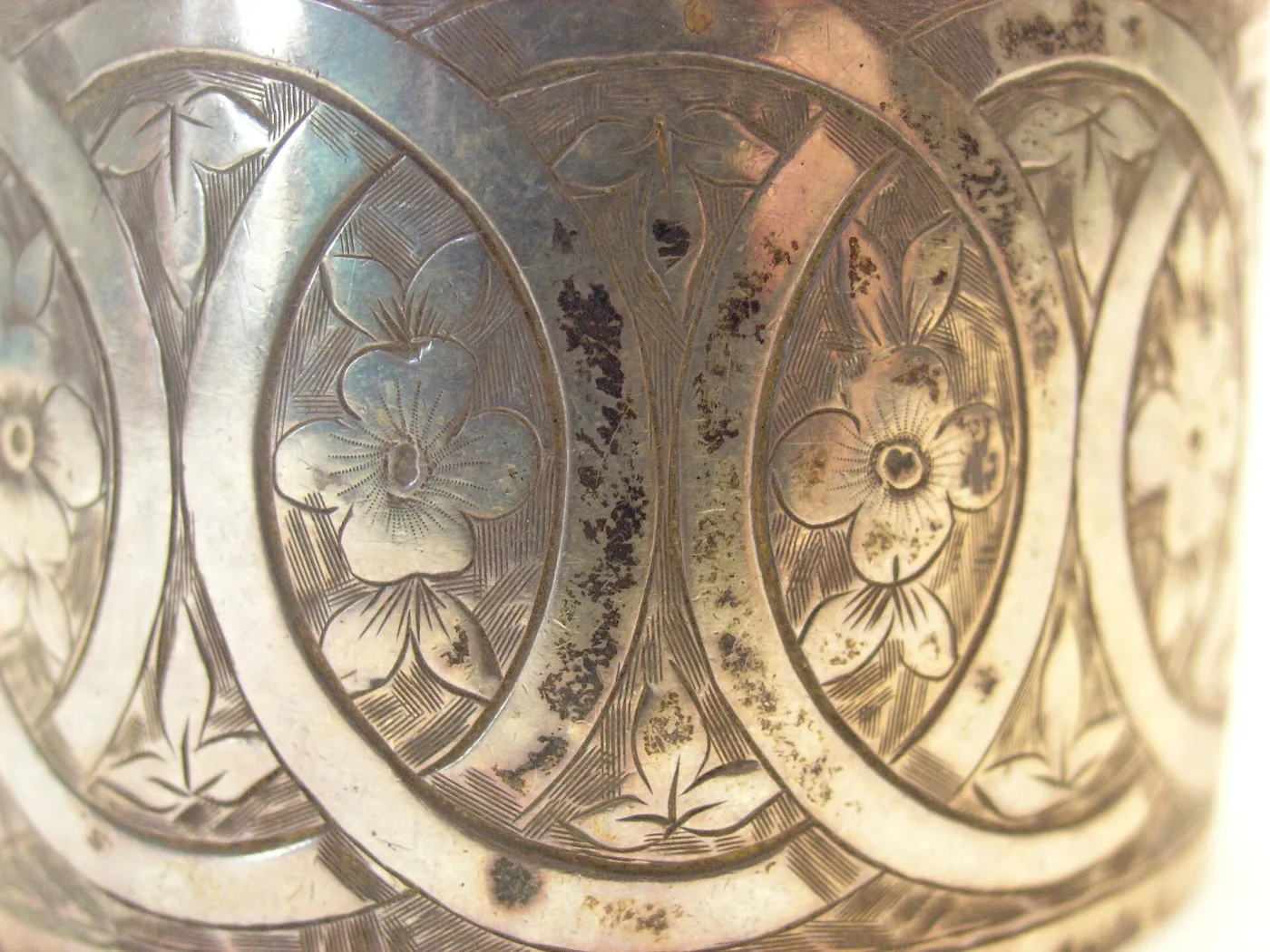 Close view of engraved silver showing linked ovals enclosing four-petalled flowers cut against a finely cross-hatched background