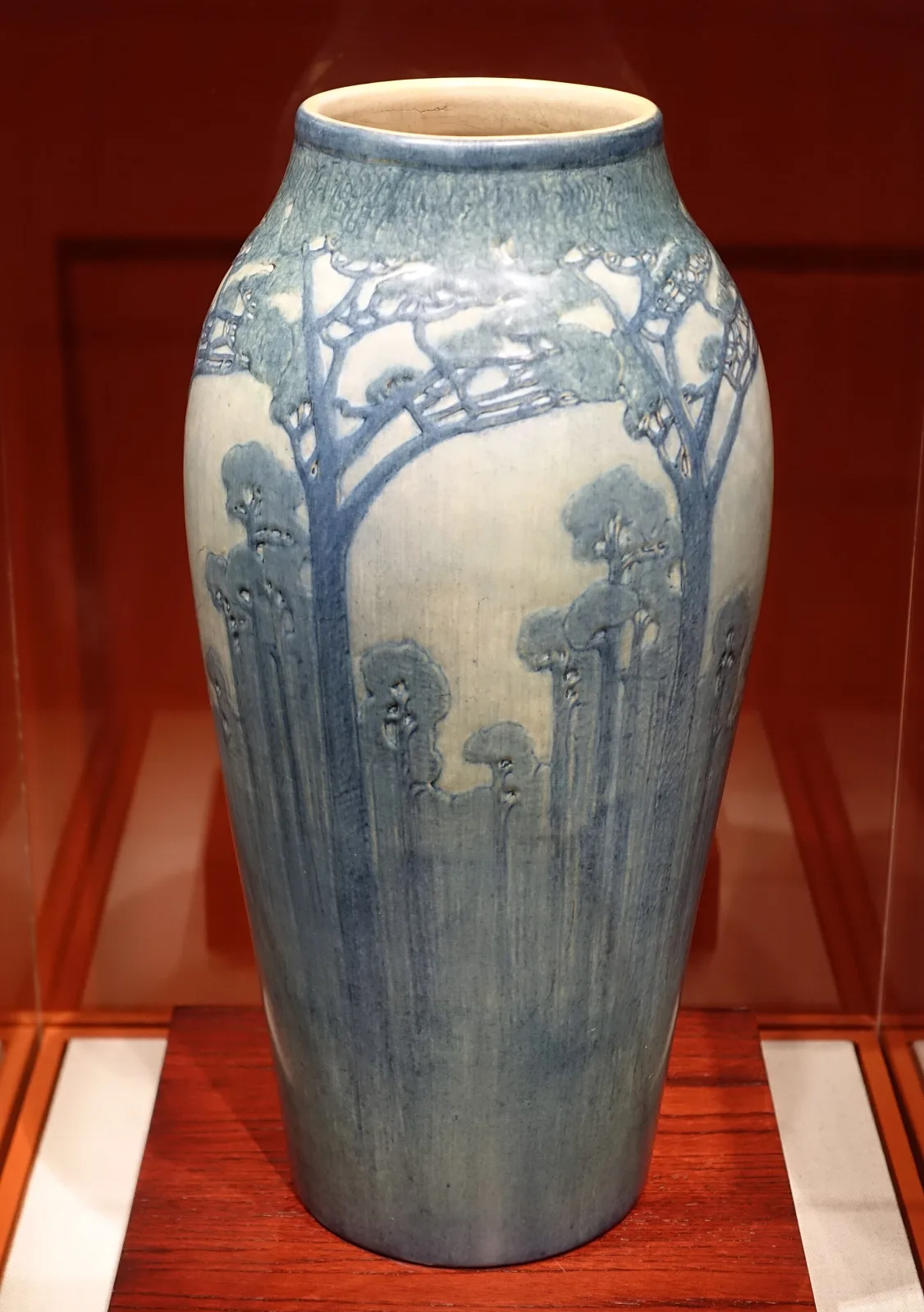 Tall ovoid vase in soft blue and grey matte glaze, carved and painted with a stand of slender pine trees rising the full height of the body against a paler sky