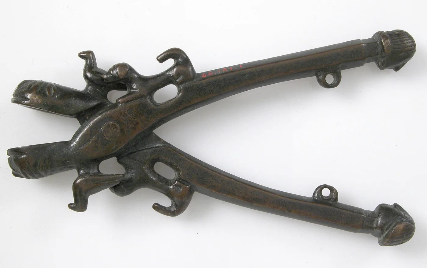 Cast bronze nutcracker with two long tapering arms hinged at a head formed as opposed animal jaws, a small cast creature perched above the pivot