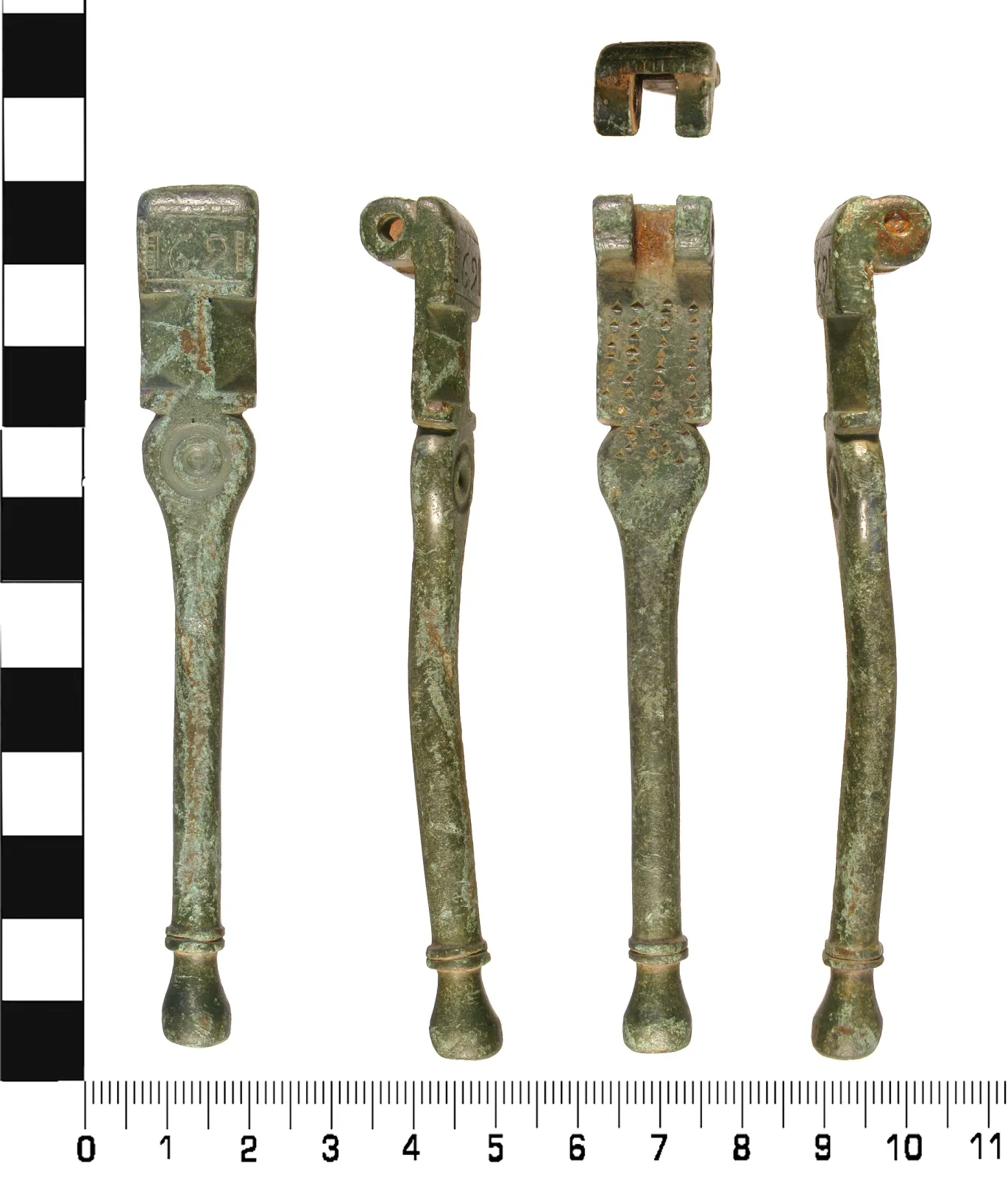 Four views of a single copper-alloy nutcracker arm against a centimetre scale, its head engraved with the numerals 1691, with the detached hinge fragment shown above