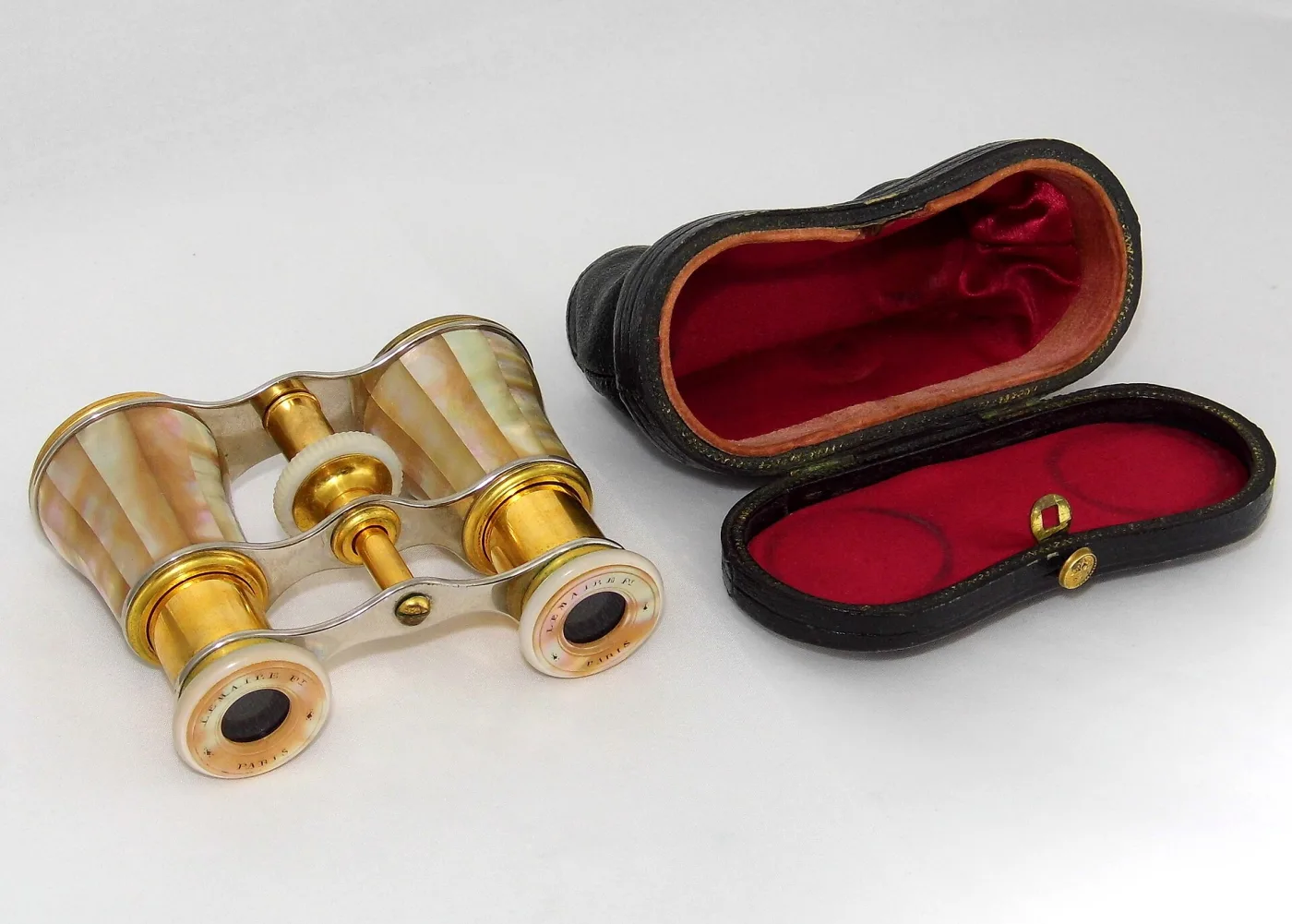 Mother-of-pearl and gilt opera glasses lying beside their fitted leather case with a red silk lining