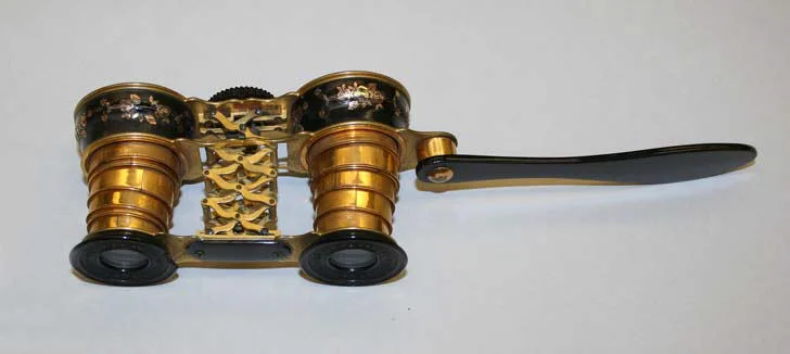Gilt opera glasses with black enamel bands and pierced bridge, a long black handle extending to one side
