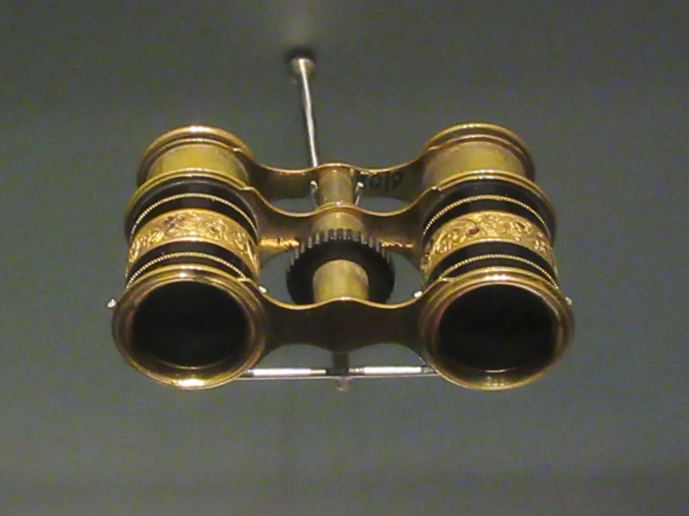 Small gilt opera glasses with dark bands and chased floral ornament, displayed on a museum mount