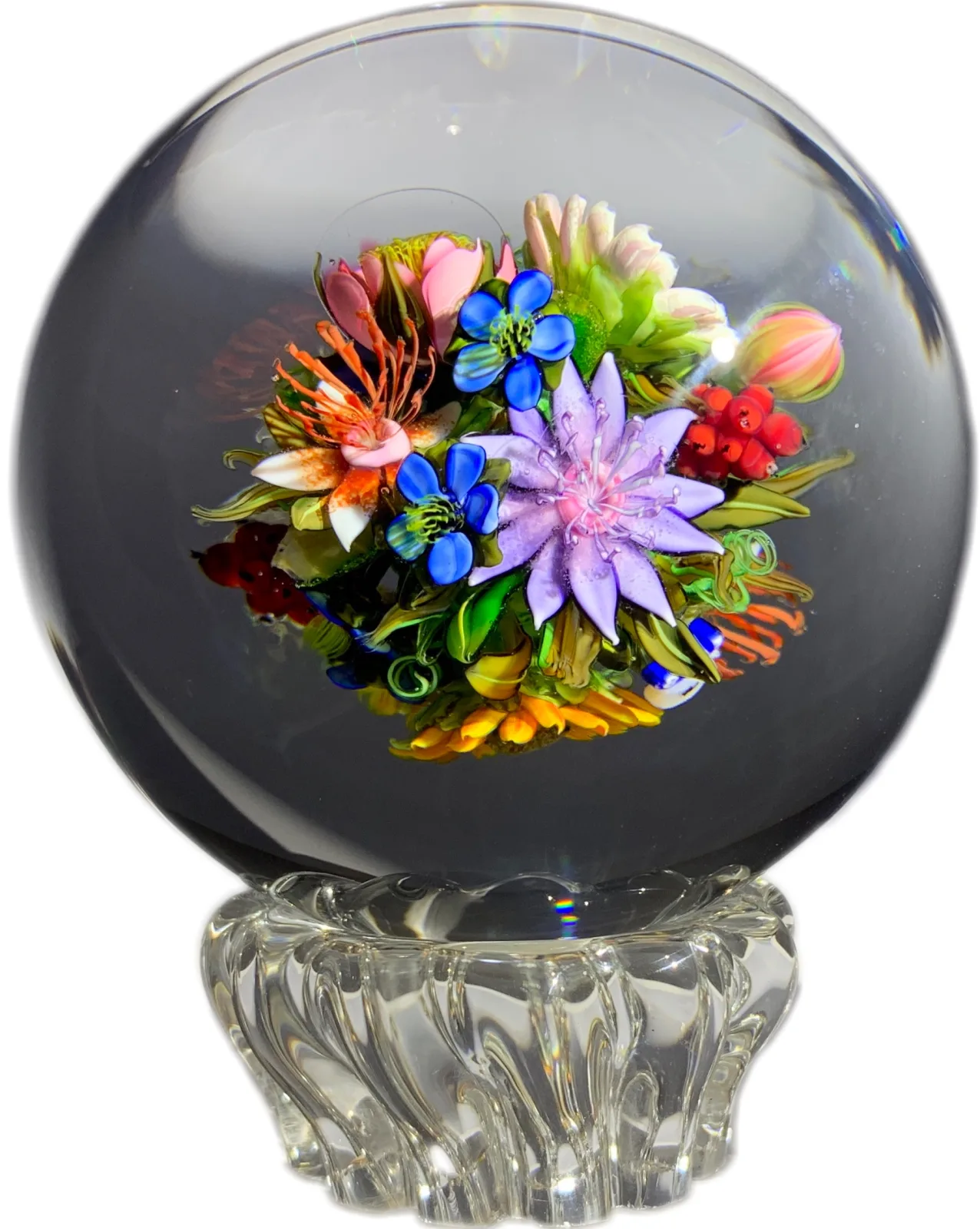 Spherical paperweight on a fluted clear glass foot, enclosing a dense lampwork bouquet of many-coloured flowers and buds viewable from every side