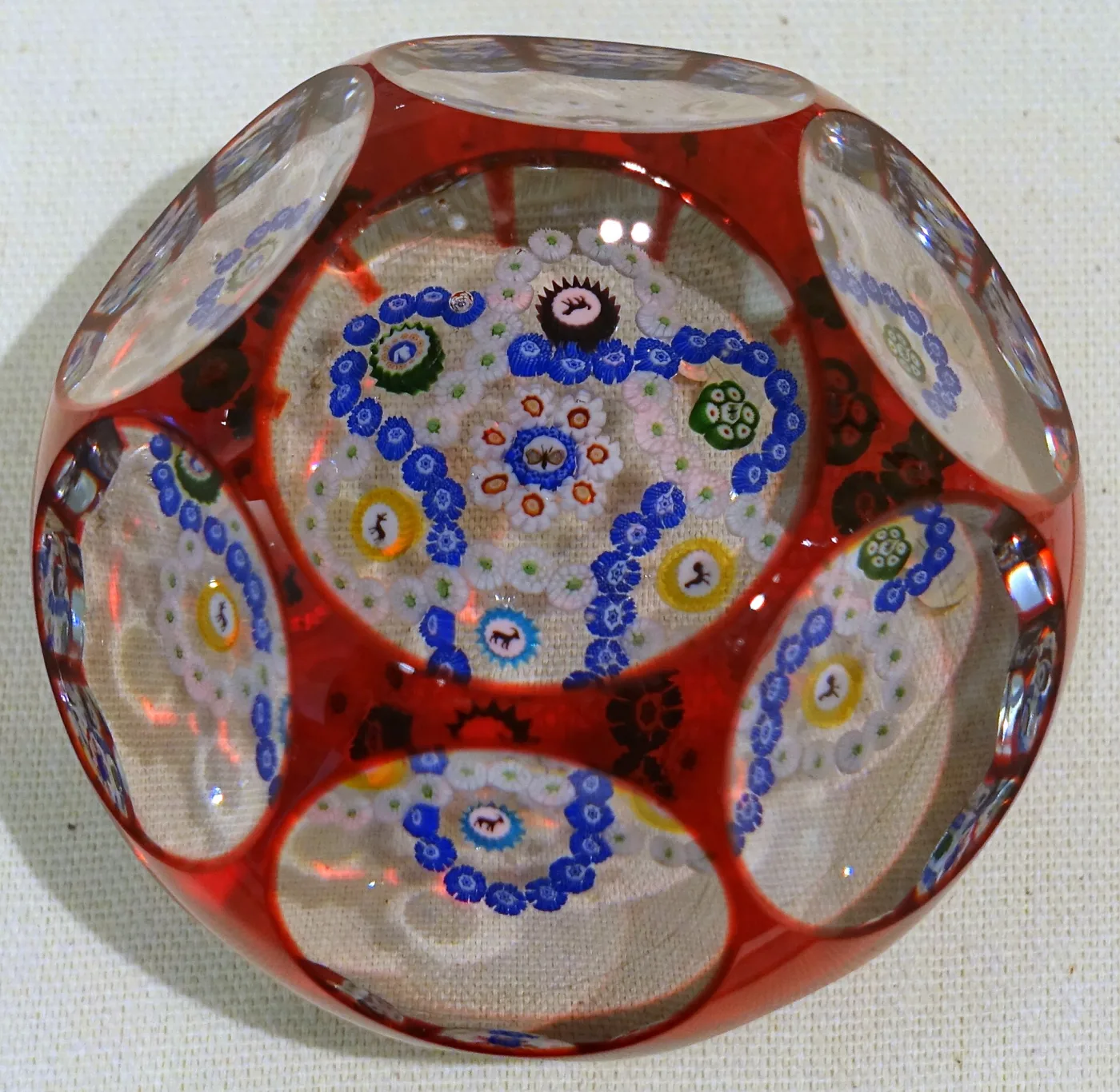 Paperweight cased in opaque red glass which has been cut through with one circular window on top and five round windows around the sides, each revealing concentric millefiori canes inside
