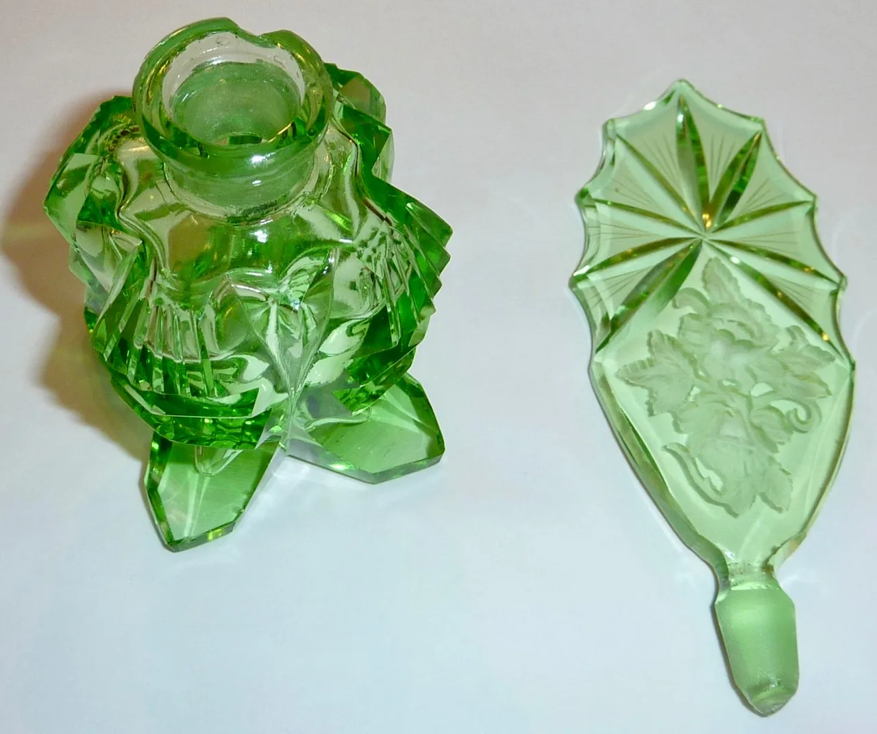 Green cut-glass perfume bottle lying on its side beside its separate large flat stopper, which is shaped like a shield and carries an intaglio-cut flower spray, its plug end frosted