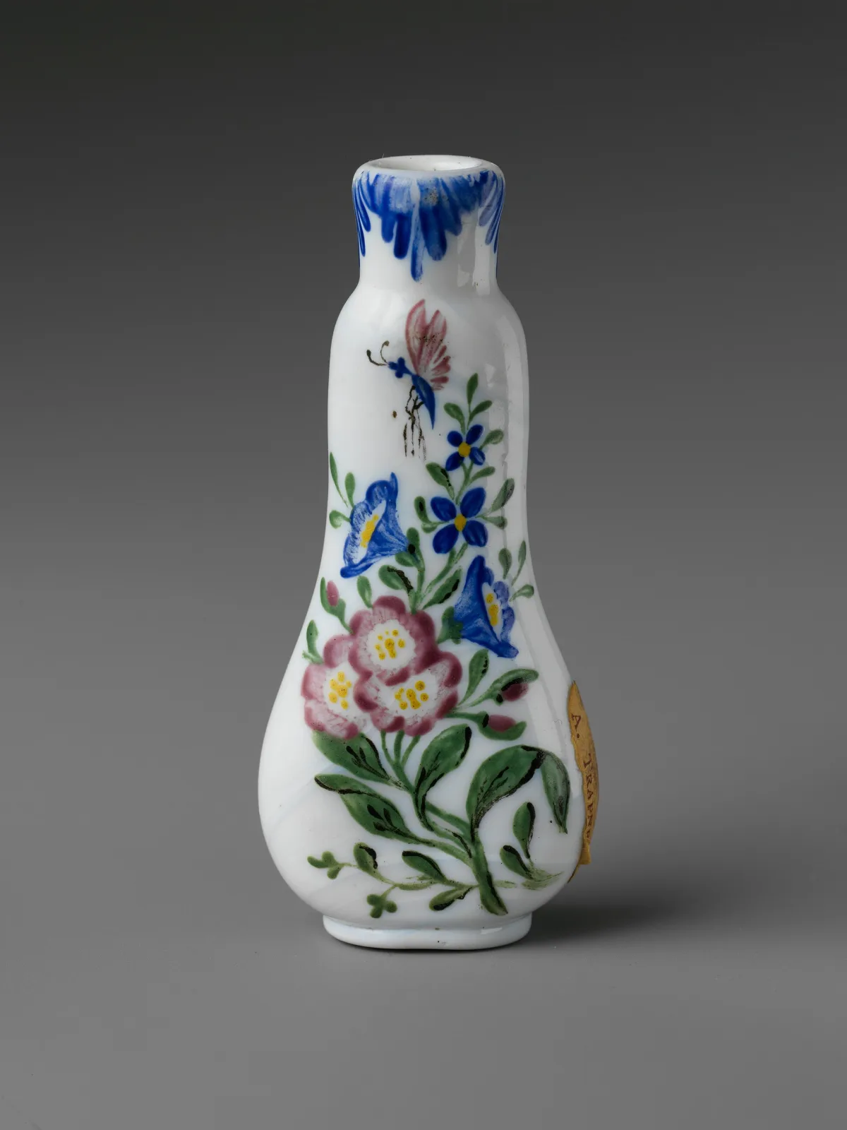 Small opaque white glass bottle of flattened baluster shape, enamelled with pink and blue flowers on green stems, the neck rim painted with blue feathering and an old paper label stuck to one side