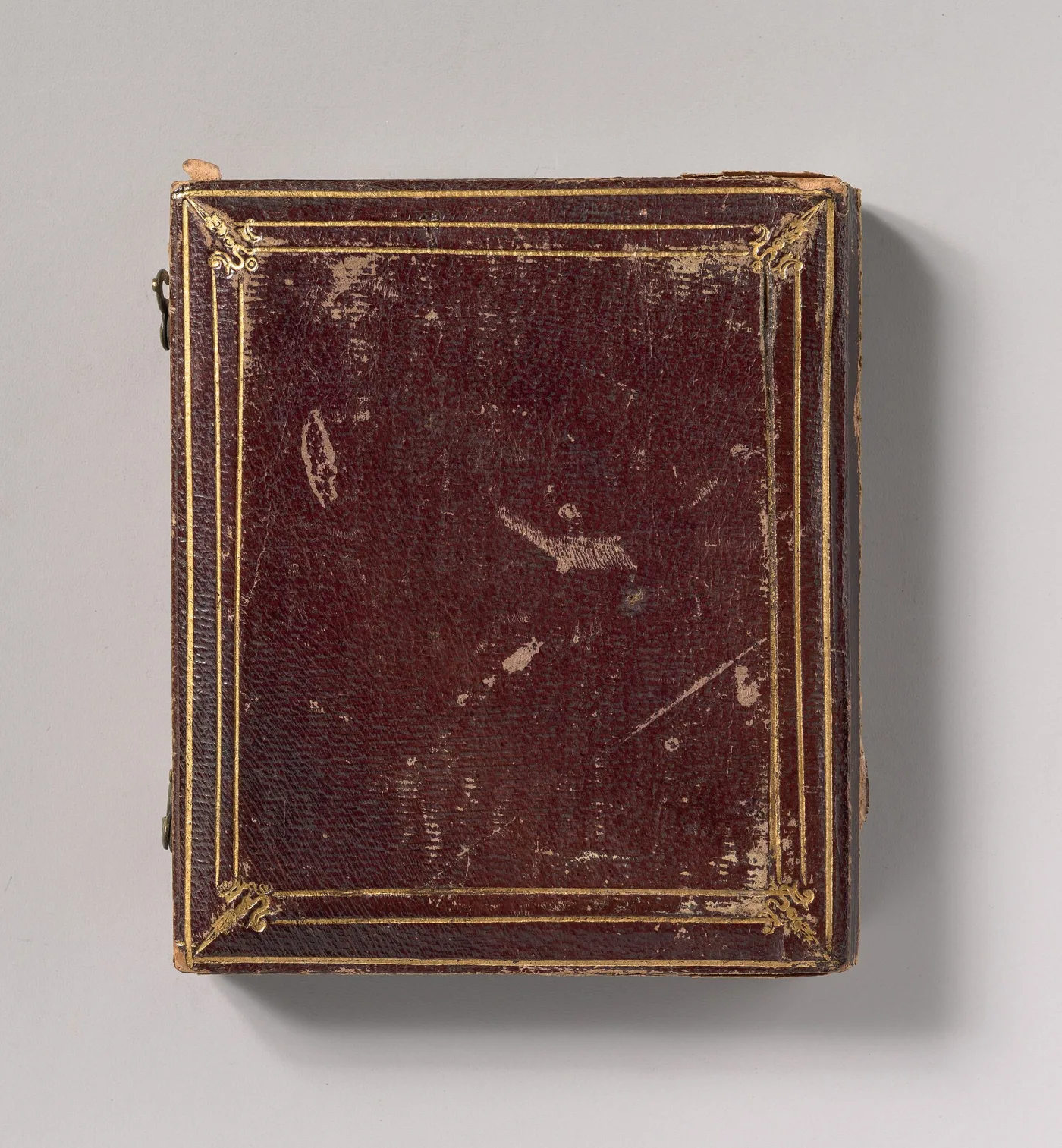Closed rectangular case of dark red-brown leather over wood, its front panel blind-tooled with a decorative border and worn pale at the corners and along the hinge