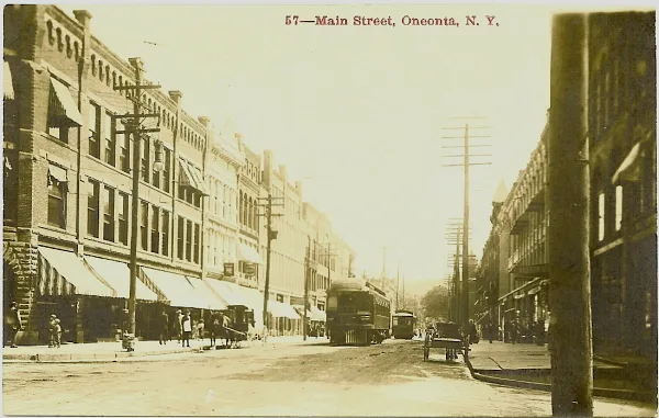 Sepia real photo postcard of a main street with a streetcar and horse-drawn wagon, captioned 57 — Main Street, Oneonta, N. Y. along the top edge