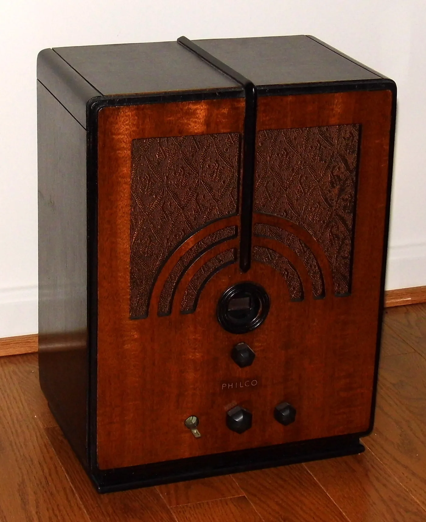 Upright wooden radio with a squared top, a rainbow-arc grille cut into figured veneer, a round dial and three faceted knobs