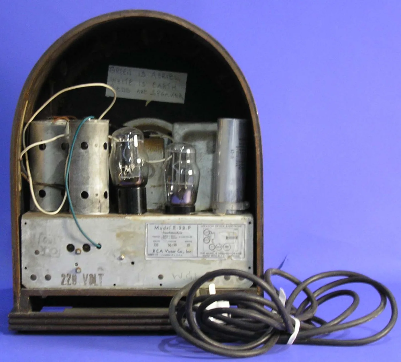 Back of an arched wooden radio with the cover removed, showing two glass tubes, metal cans, a paper label reading Model R-28-P and a coiled mains cable