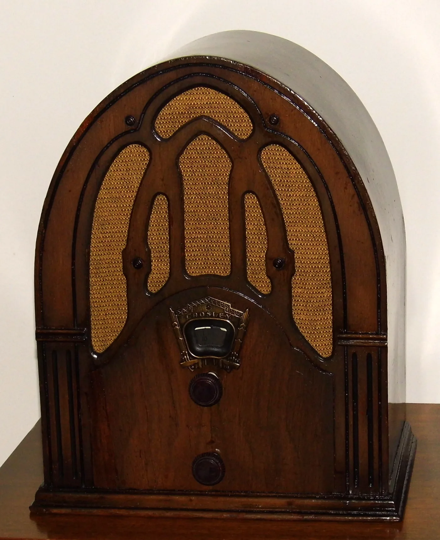 Tall arched wooden cathedral radio with a five-lobed cloth grille, a small brass-framed dial and two knobs