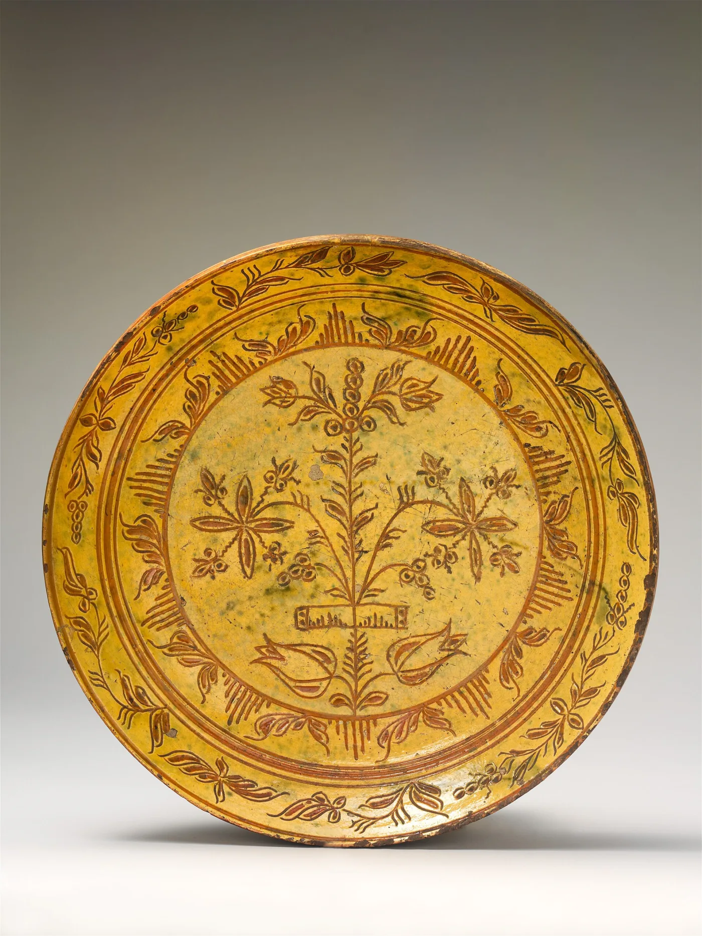 Yellow-slipped plate incised with a flowering plant rising from an urn inside a dense border of repeated leaves