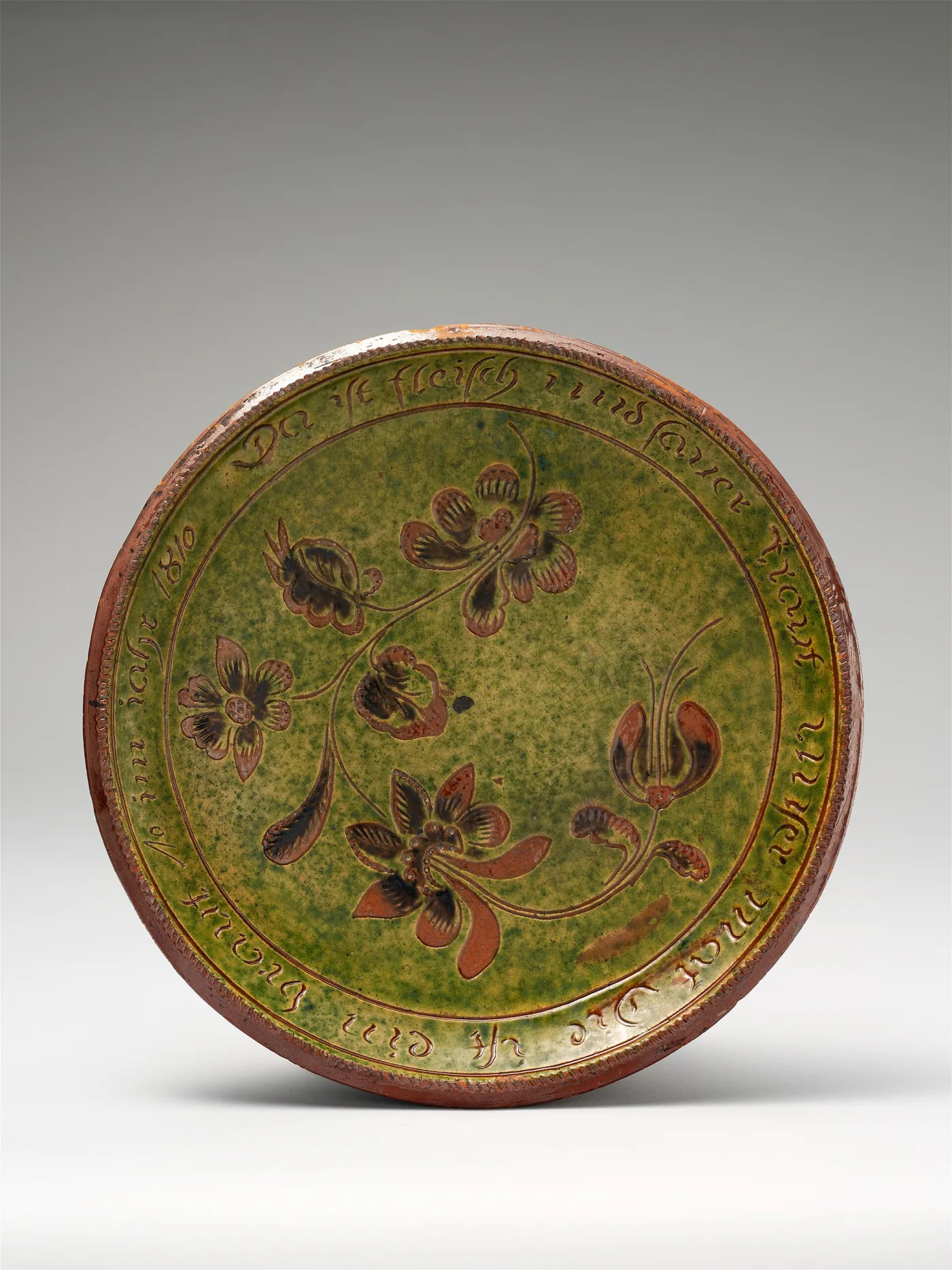 Plate with a mottled copper-green ground, incised flowers in red-brown, and a German inscription running around the rim