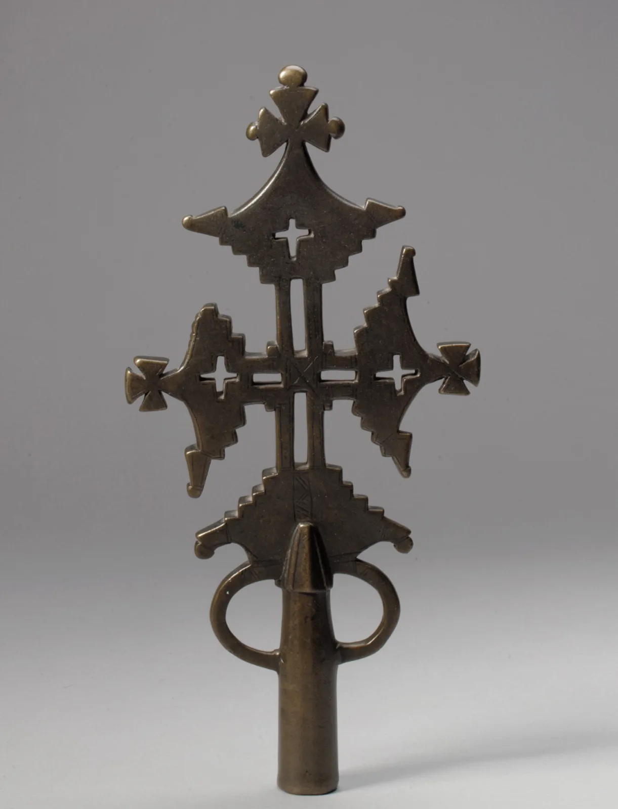 Brass processional cross with flared arms ending in stepped points, small crosses at the arm ends, a pierced roundel below the shaft and a socket at the foot for a pole