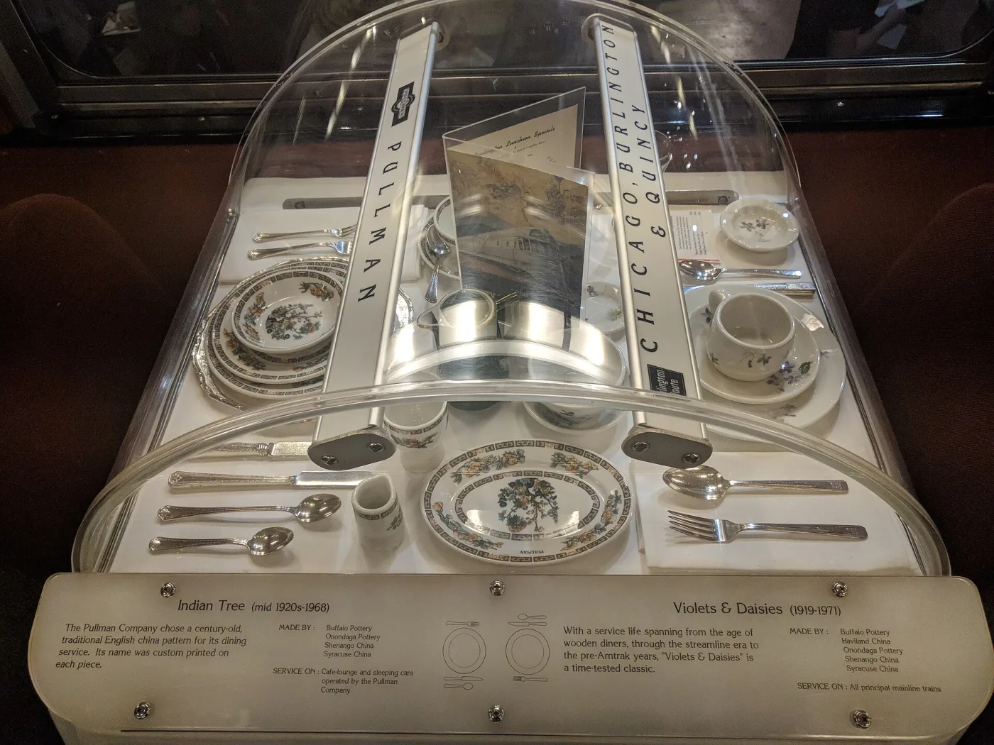 Museum case of Pullman Company china in two floral patterns, with an interpretive label listing the pattern names, date ranges and the potteries that produced them