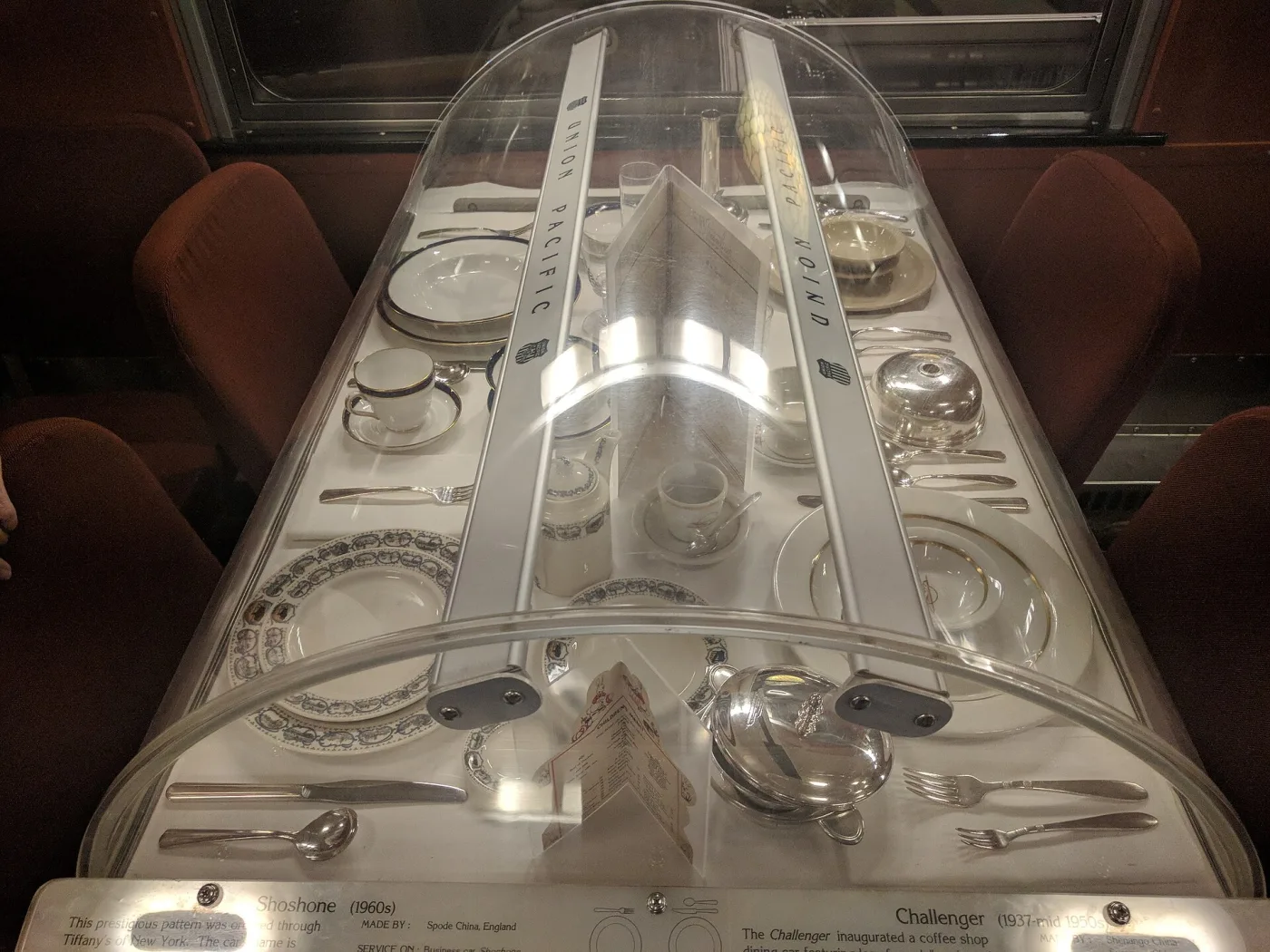Museum case of Union Pacific dining car china with delicate printed borders, seen through the curved cover of a display cabinet