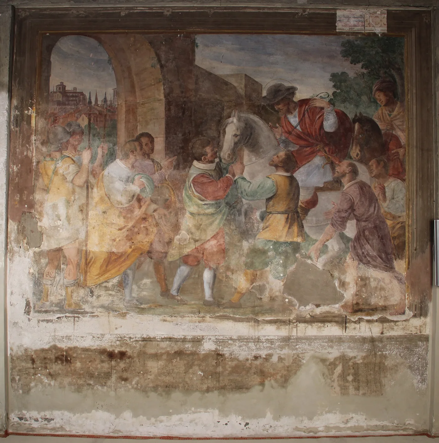 Wall painting of a rider entering a city gate, its surface dulled by grey haze and white salt bloom, with paint losses through the lower half and a broad stain along the dado beneath