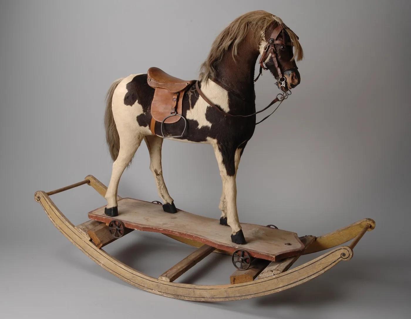 The same hide-covered horse and wheeled platform, now seated inside a curved wooden bow rocker frame