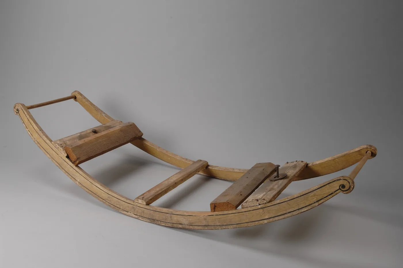 A bare wooden bow rocker: two long curved runners with scrolled ends joined by cross-boards, with a turned rail across one end and no horse fitted
