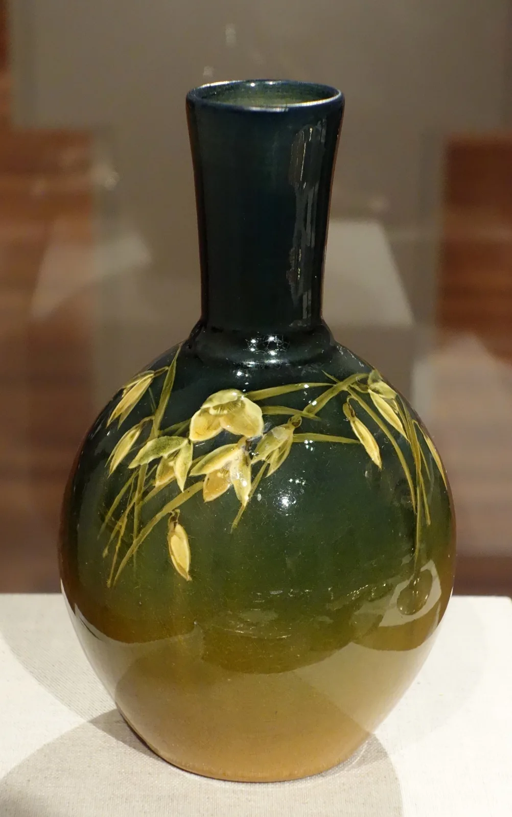 Tall vase with a swelling base and long neck, glazed in soft green shading to blue-green, painted with pale yellow daffodils and slender leaves under a matte, non-reflective surface